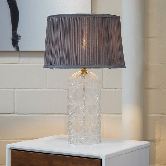 Textured glass table lamp with pleated grey shade, lit on a bedside nightstand