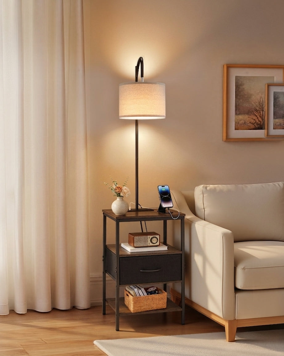 Floor lamp with side table — 59 in black metal frame with linen drum shade, drawer and open shelf, lit beside a cream armchair