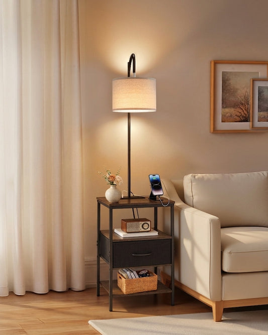 Floor lamp with side table — 59 in black metal frame with linen drum shade, drawer and open shelf, lit beside a cream armchair