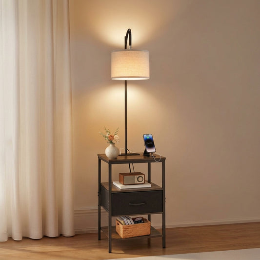 Floor lamp with side table and shelves — 59 in black metal frame with linen drum shade, lit, fabric drawer and open shelf, phone charging on the tabletop